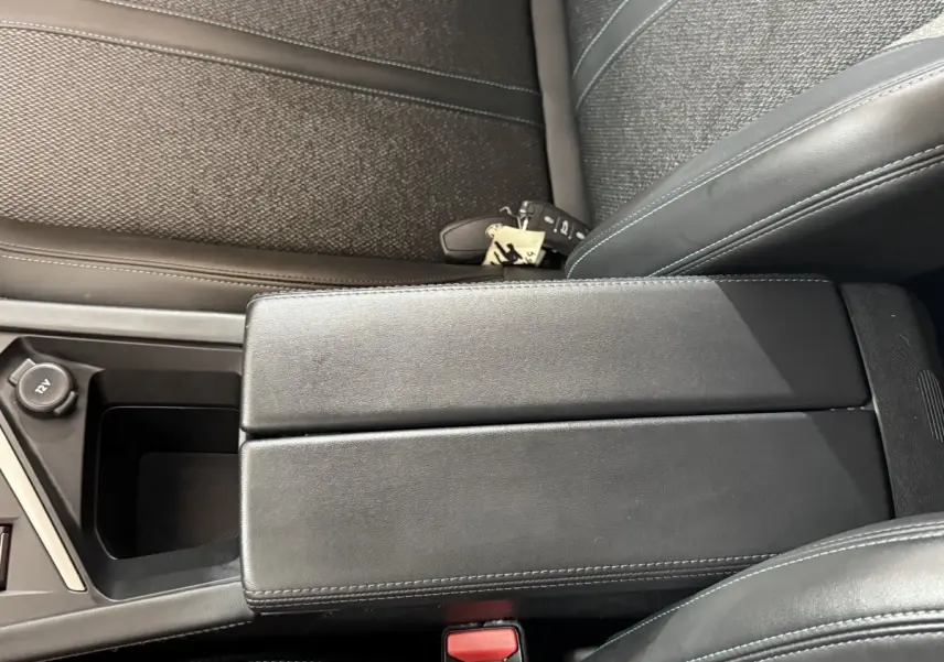 Vue rapprochée de l'accoudoir central noir et des sièges en tissu gris foncé à coutures bleues dans une Peugeot 308 2023.