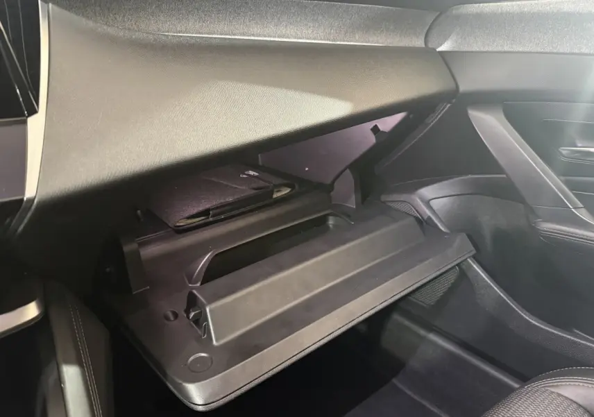 Vue intérieure côté passager du coffre à gants ouvert de la Peugeot 308 bleu, avec un carnet noir à l'intérieur.