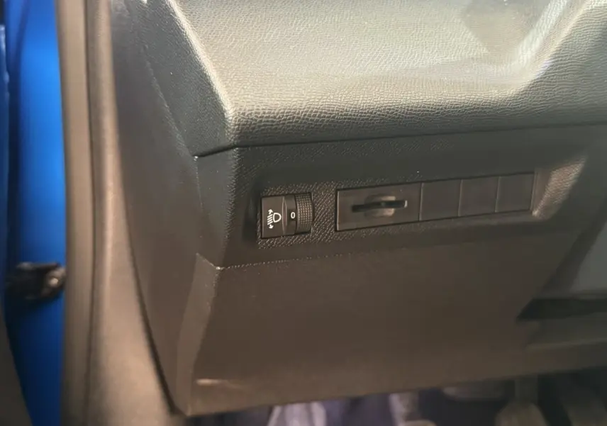 Détail du panneau de réglage des phares sur la partie inférieure gauche du tableau de bord d'une Peugeot 308 bleu 2023.