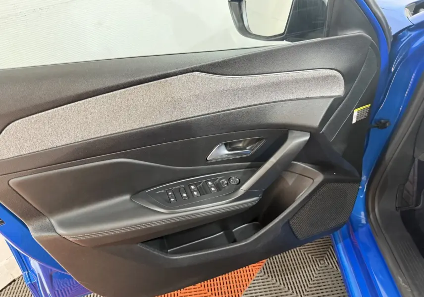 Vue intérieure côté gauche de la porte avant bleu vif d'une Peugeot 308 2023 avec commandes électriques et garniture grise.