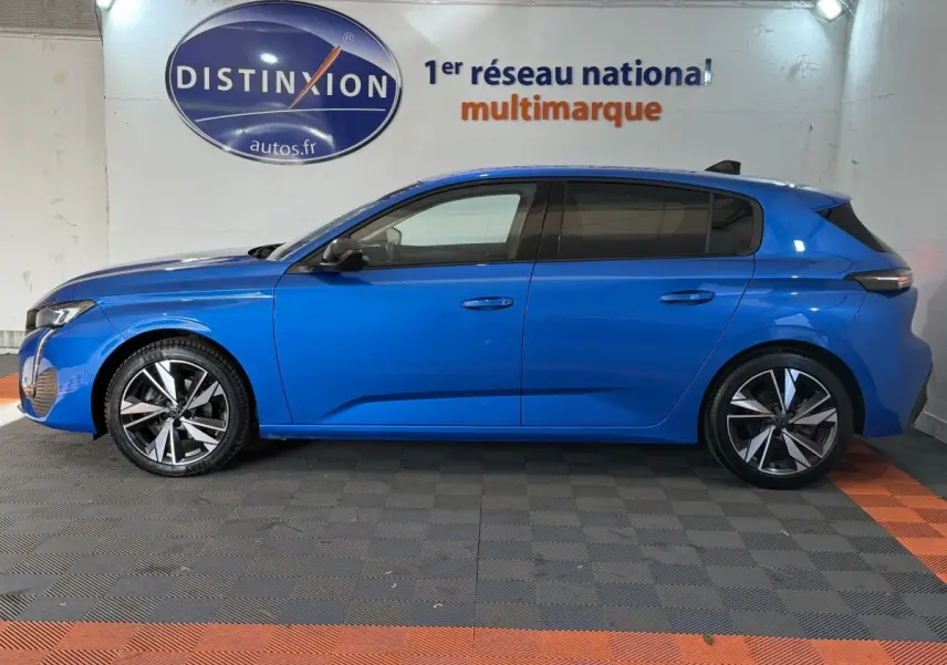 Profil côté gauche d'une Peugeot 308 bleu 2023 avec jantes alliage et vitres teintées, en intérieur showroom.