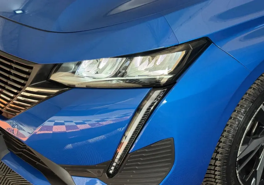 Gros plan sur l'avant droit bleu vif de la Peugeot 308 2023, mettant en valeur le phare LED et la calandre distinctive.