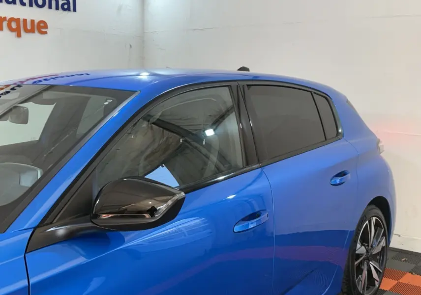 Vue latérale gauche d'une Peugeot 308 bleu vif avec rétroviseur noir brillant et vitres teintées.