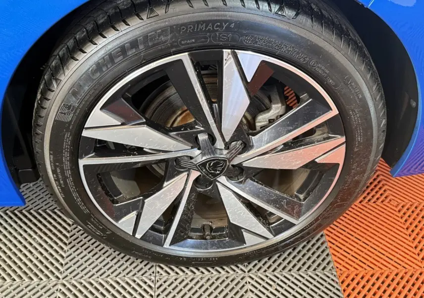 Gros plan sur la roue avant gauche d’une Peugeot 308 bleu 2023 avec jante alliage bicolore et pneu Michelin.