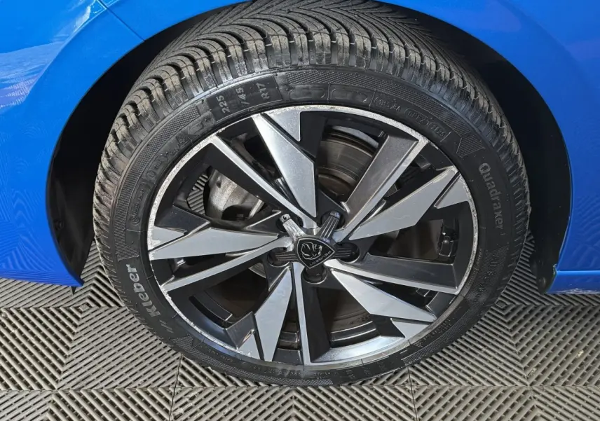 Gros plan sur la roue avant droite d’une Peugeot 308 bleu, avec jante alliage noire et argentée au design moderne.