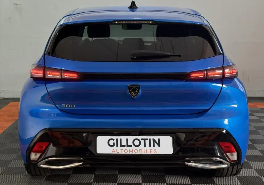 Vue arrière d’une Peugeot 308 bleu 2023 avec feux LED allumés et double sortie d’échappement chromée.