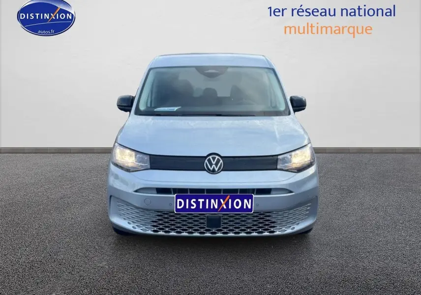 Vue de face d'un Volkswagen Caddy gris argent 2025 avec calandre noire et phares allumés.