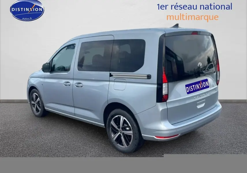 Volkswagen Caddy gris argent vu en 3/4 arrière droit, avec vitres teintées et jantes alliage noires.
