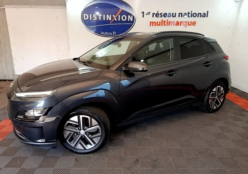 Hyundai Kona électrique 2021 gris foncé en 3/4 avant droit, avec jantes spécifiques et rails de toit noirs visibles.