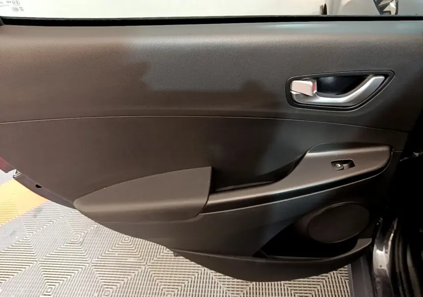 Vue intérieure côté gauche de la porte avant noire du Hyundai Kona électrique avec poignée argentée et commande de vitre.