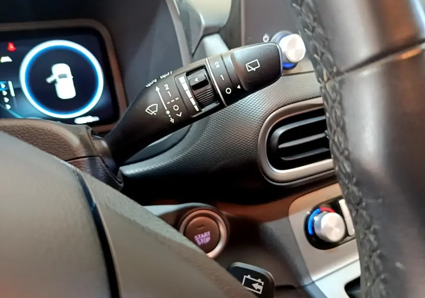 Vue intérieure rapprochée du volant cuir et des commandes de la Hyundai Kona électrique, avec tableau de bord et bouton start/stop visibles.