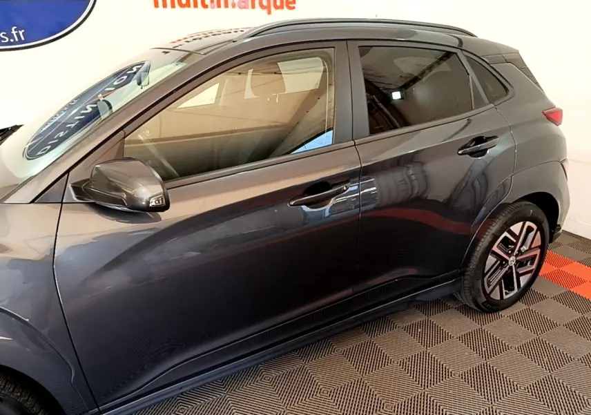 Vue latérale côté gauche d'une Hyundai Kona électrique 2021 gris foncé avec jantes spécifiques et rétroviseurs assortis.