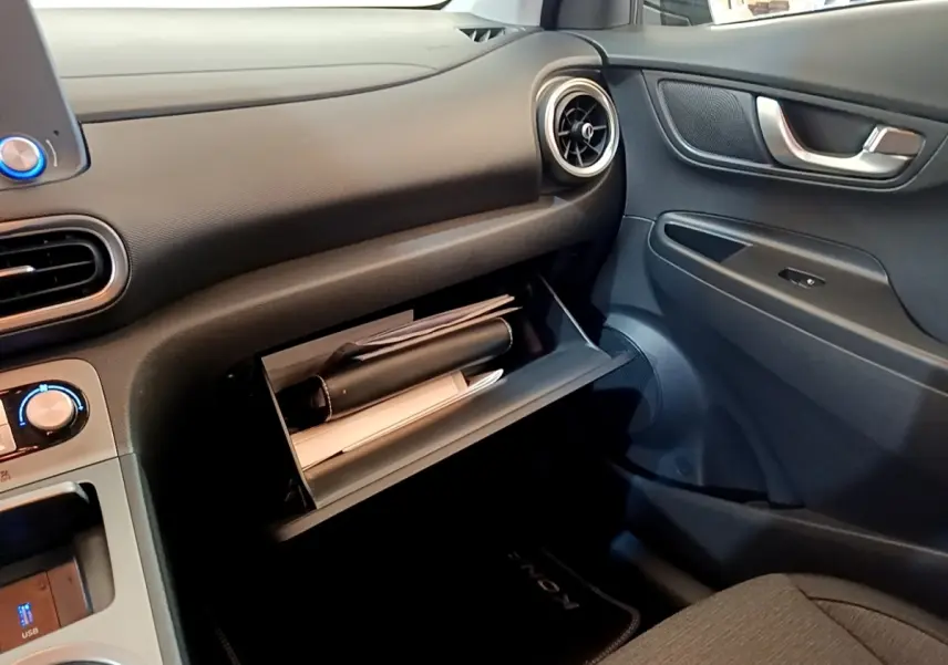 Vue intérieure côté passager du tableau de bord noir d'une Hyundai Kona électrique avec boîte à gants ouverte contenant des documents.