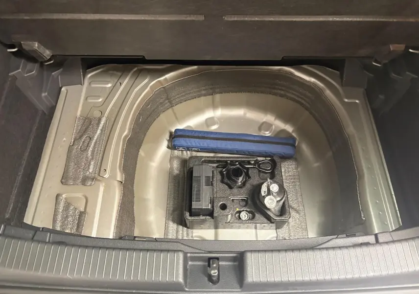 Coffre ouvert du Volkswagen T-Cross 2024, vue sur le compartiment à roue de secours avec kit de dépannage visible.