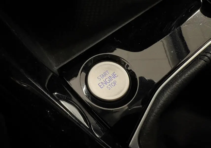 Bouton start/stop moteur argenté sur console noire brillante du Volkswagen T-Cross 2024 finition VW Edition.