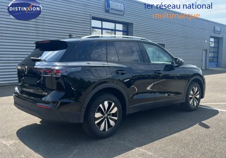 Vue 3/4 arrière droite d'un Volkswagen Tiguan noir Grenadilla métallisé stationné devant un bâtiment industriel.
