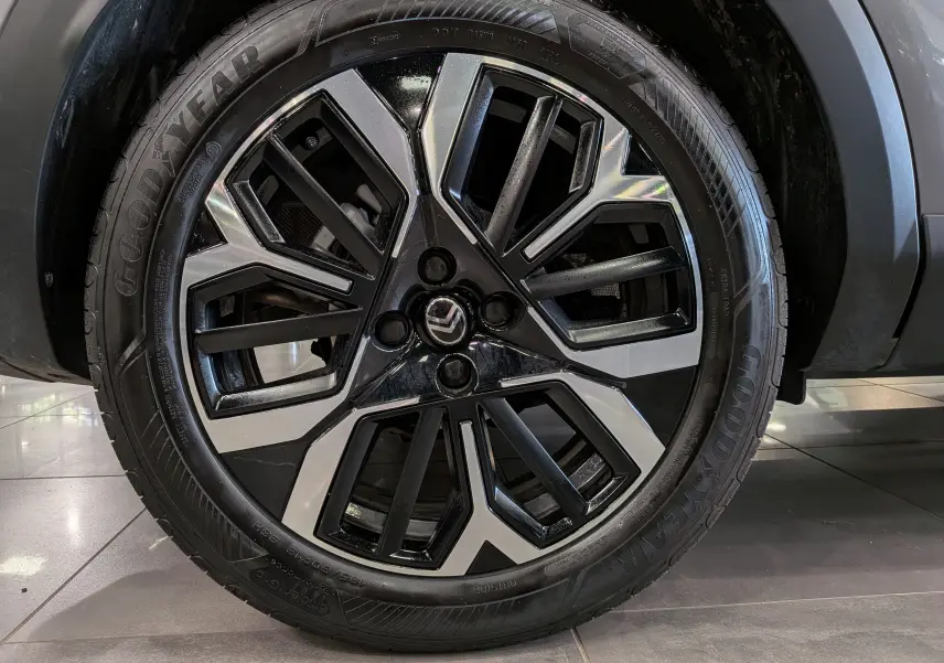 Gros plan sur la jante bicolore noire et argentée avec logo Citroën, montée sur un pneu Goodyear, partie avant droite du C4 gris Mercury.