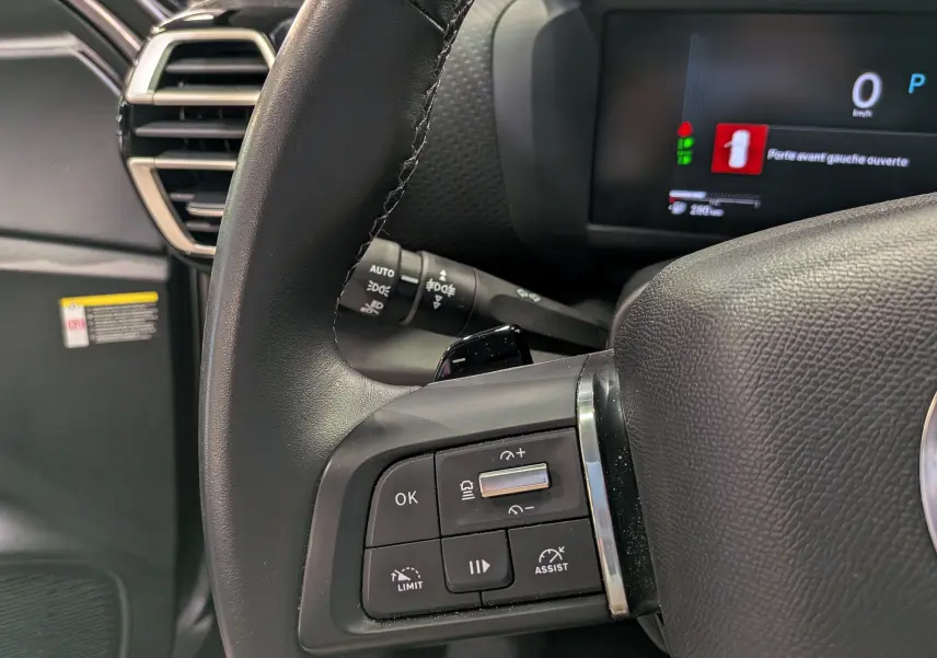 Gros plan sur le volant côté gauche de la Citroën C4 hybride 2025 avec commandes intégrées et tableau de bord numérique.