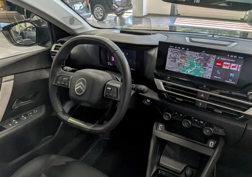 Vue intérieure côté conducteur du Citroën C4 hybride 2025, volant cuir noir et écran tactile avec navigation affichée.