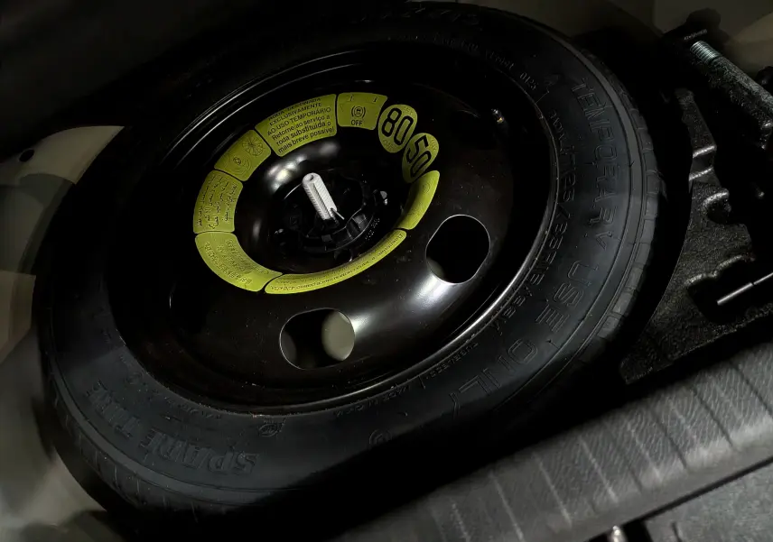 Gros plan sur la roue de secours noire avec étiquettes jaunes dans le coffre d'une Citroën C4 Hybride gris Mercury.