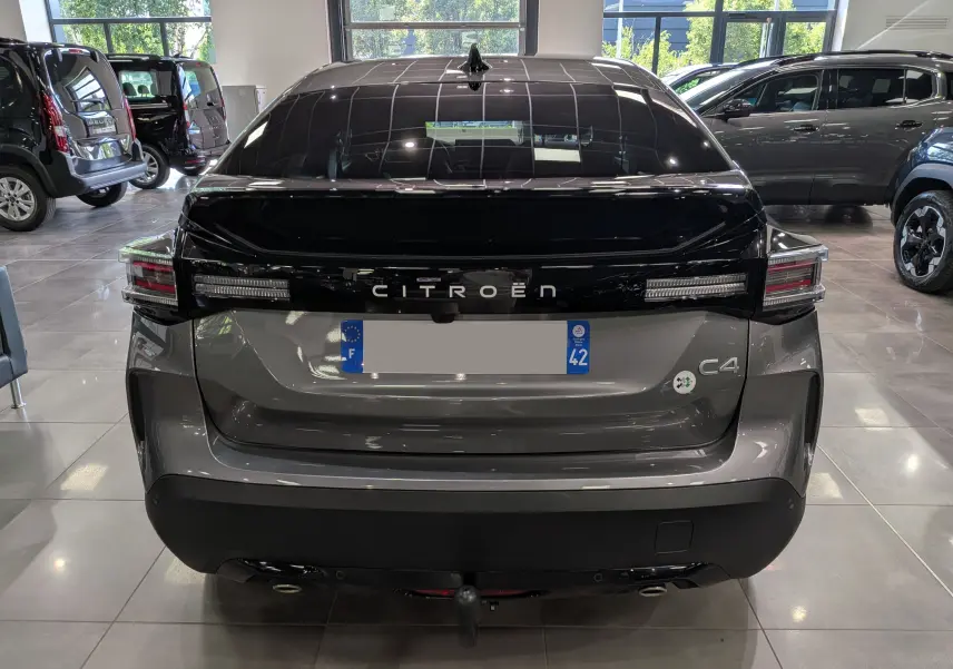 Vue arrière d'une Citroën C4 hybride gris Mercury avec toit noir brillant et feux arrière étirés en intérieur showroom.