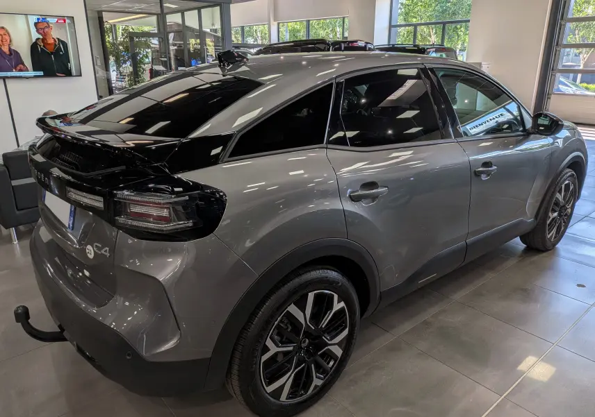 Vue 3/4 arrière droite d'une Citroën C4 hybride gris Mercury avec toit noir brillant et jantes bicolores en concession.