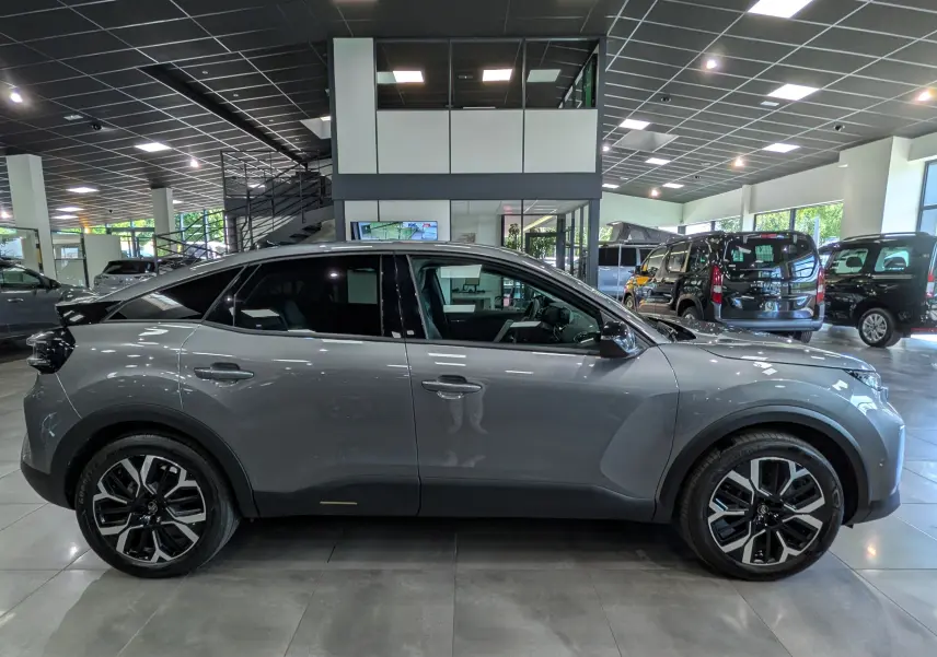 Vue de profil côté gauche d'une Citroën C4 hybride gris Mercury en intérieur, avec jantes noires et toit noir contrastant.