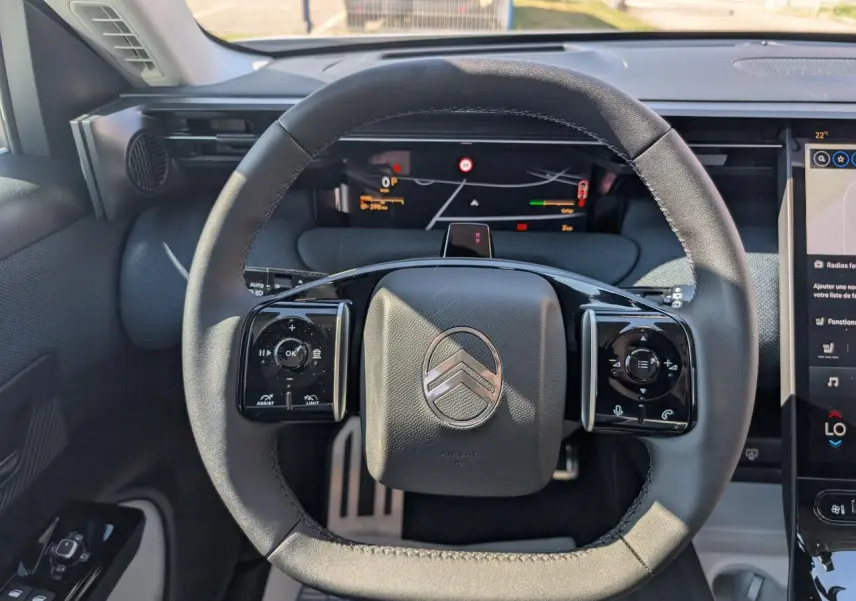 Vue rapprochée du volant noir mat au logo Citroën, avec tableau de bord numérique et écran tactile latéral.