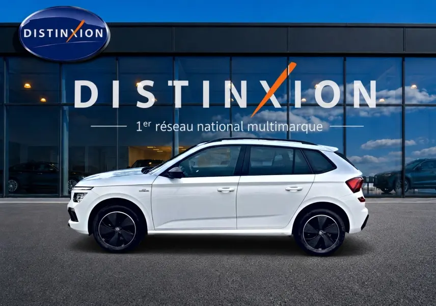 Profil droit d’un Skoda Kamiq blanc nacré 2026 avec jantes noires et toit panoramique devant une vitrine Distinxion.
