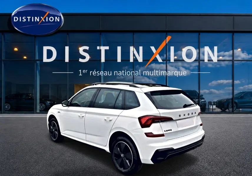 Vue 3/4 arrière droite d'un Skoda Kamiq blanc nacré avec jantes noires devant un showroom Distinxion.