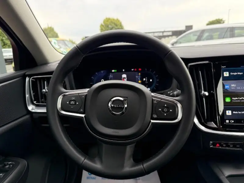 Volant noir de Volvo S60 2024 hybride essence, vue frontale du poste de conduite avec écran tactile et tableau de bord numérique.