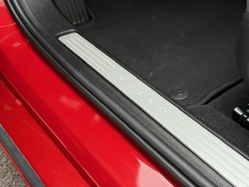 Gros plan sur la plaque de seuil de porte avec logo Volvo, côté intérieur d'une Volvo S60 rouge fusion métallisé 2024.