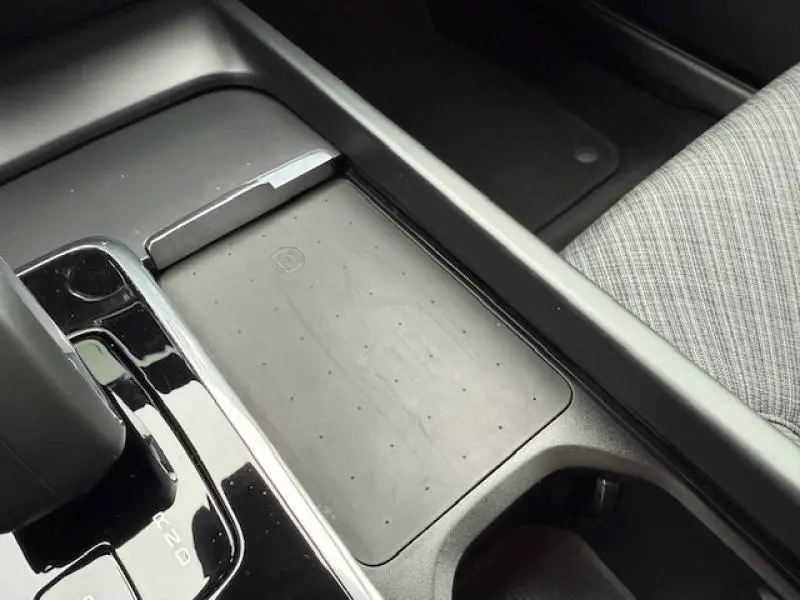 Vue rapprochée de la console centrale noire du Volvo S60 2024, mettant en valeur le chargeur sans fil et la sellerie grise à motifs.