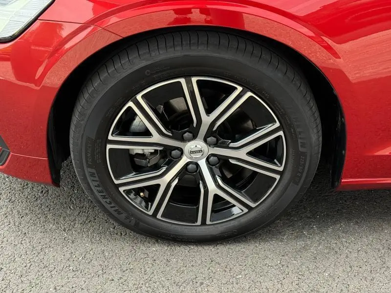 Gros plan sur la roue avant gauche d'une Volvo S60 2024 Rouge Fusion Métallisé avec jante alliage noire et argentée.