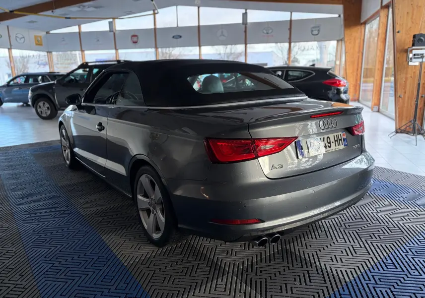 Audi A3 Cabriolet gris vue 3/4 arrière droit avec capote noire dans un showroom lumineux.