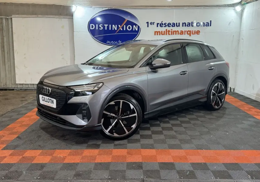 Audi Q4 E-TRON gris foncé en 3/4 avant droit, avec jantes noires et détails noirs brillants visibles en intérieur showroom.