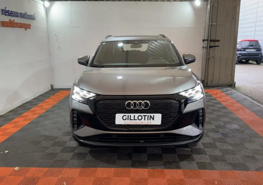 Audi Q4 E-TRON gris foncé vu de face dans un garage avec calandre noire et phares LED allumés.