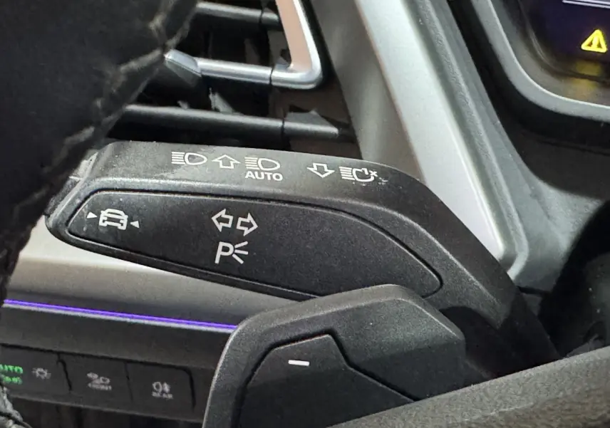 Gros plan sur la commande de clignotants et feux, volant noir partiellement visible, intérieur gris foncé de l'Audi Q4 E-TRON.