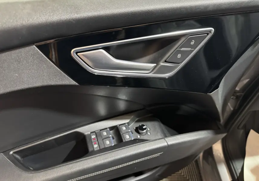 Gros plan sur la porte côté conducteur de l'Audi Q4 E-TRON gris foncé, avec commandes électriques et poignée argentée.