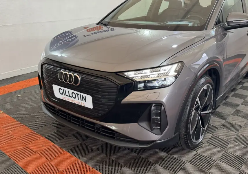 Audi Q4 E-TRON gris foncé en 3/4 avant droit, mettant en valeur sa calandre noire et ses phares LED distinctifs.