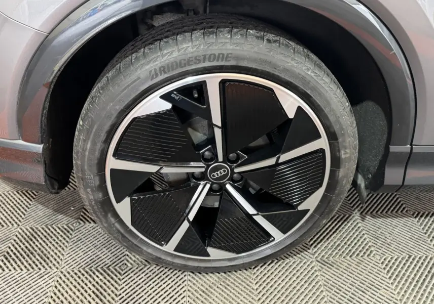 Gros plan sur la roue avant droite d’un Audi Q4 E-TRON gris foncé avec jante noire et argentée au design moderne.