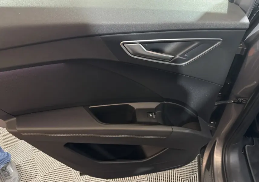 Vue rapprochée de la porte côté gauche gris foncé de l'Audi Q4 E-TRON avec poignée argentée et bouton de vitre électrique.