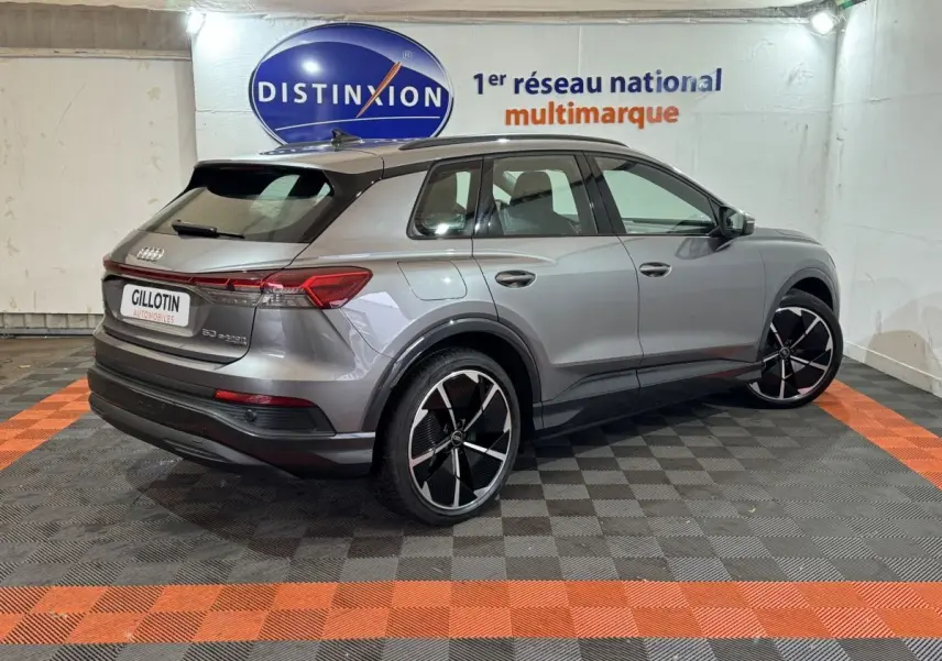 Audi Q4 E-TRON gris foncé en 3/4 arrière droit, avec jantes noires et toit panoramique visible en intérieur showroom.