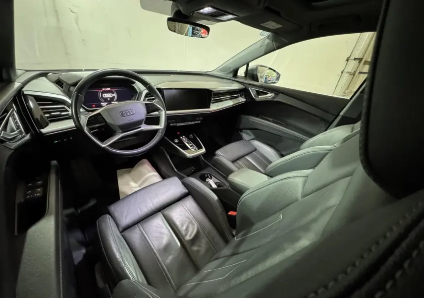 Intérieur noir de l'Audi Q4 E-TRON 50 quattro 2022, vue depuis l'arrière côté conducteur sur le tableau de bord et volant cuir multifonctions.