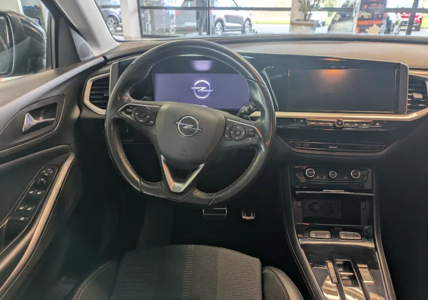 Vue intérieure avant de l'Opel Grandland 2023, tableau de bord noir avec volant multifonction et écran digital.