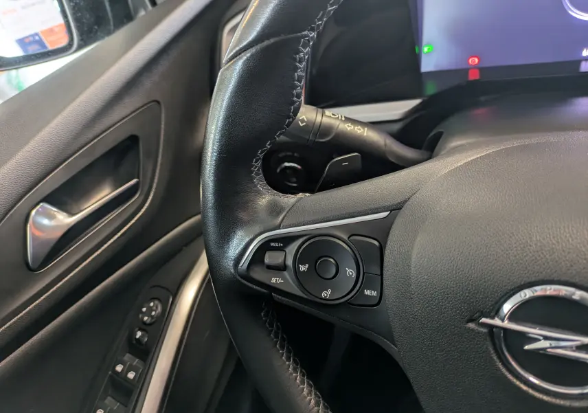 Gros plan sur le volant côté gauche noir de l’Opel Grandland 2023 avec commandes intégrées et logo Opel visible.