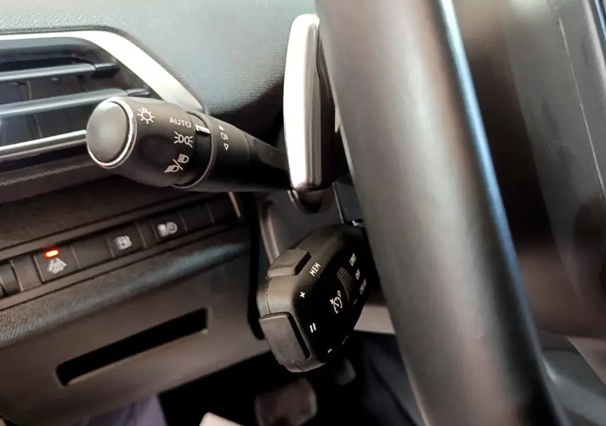 Vue rapprochée du volant noir et des commandes de phares et régulateur de vitesse du Peugeot 3008 hybride rechargeable 2021.