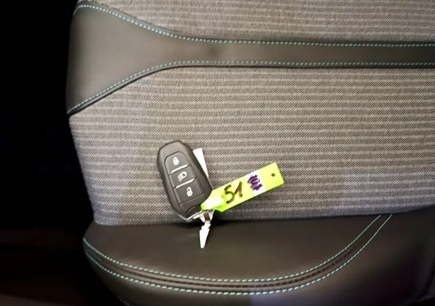 Gros plan sur la clé de voiture posée sur un siège tissu gris et cuir noir avec surpiqûres bleues, intérieur Peugeot 3008 hybride.