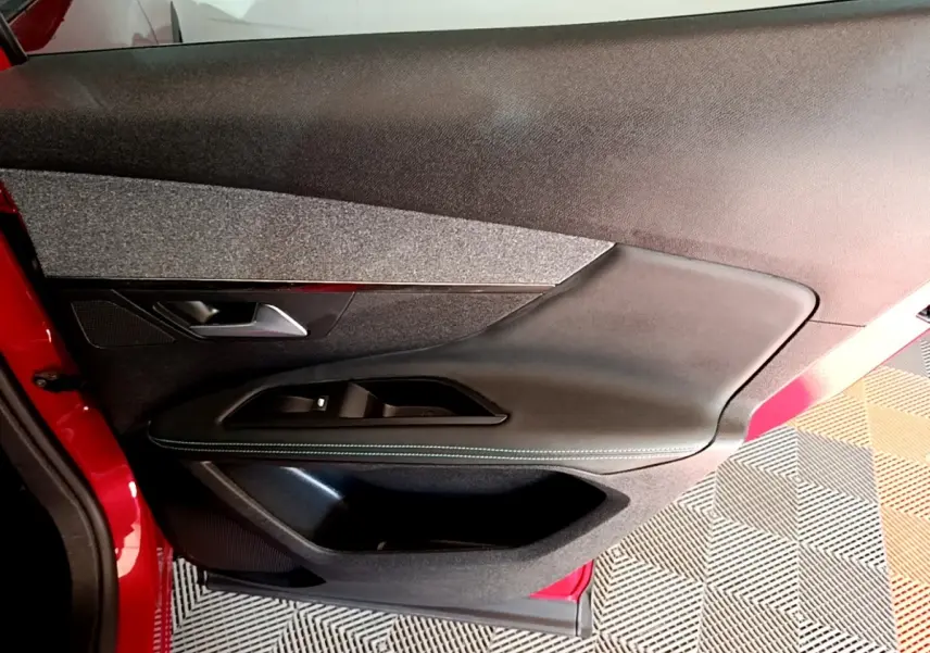 Vue intérieure côté gauche de la porte avant rouge du Peugeot 3008 1.6 HYBRID avec garniture noire et tissu gris.