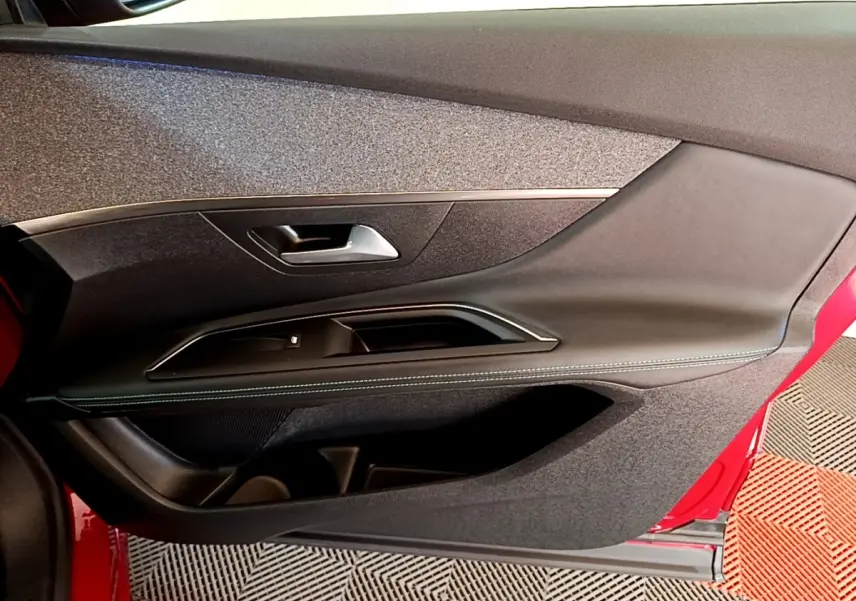 Vue intérieure côté gauche de la porte avant rouge du Peugeot 3008 avec garniture noire et insert tissu gris.